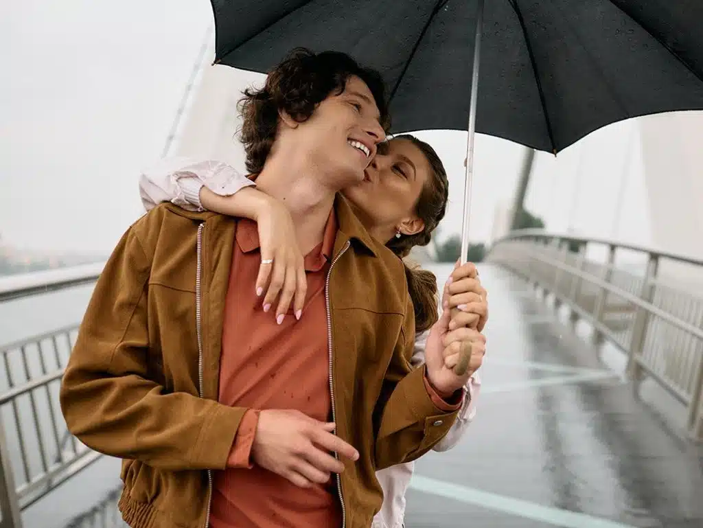 Young couple shares a tender moment while strolling through a picturesque park in the rain.